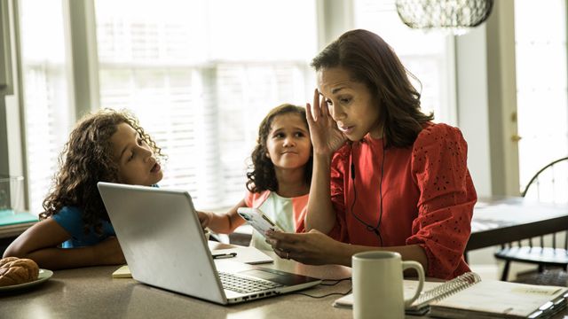 Una mujer tratando de trabajar con sus dos hijas al lado
